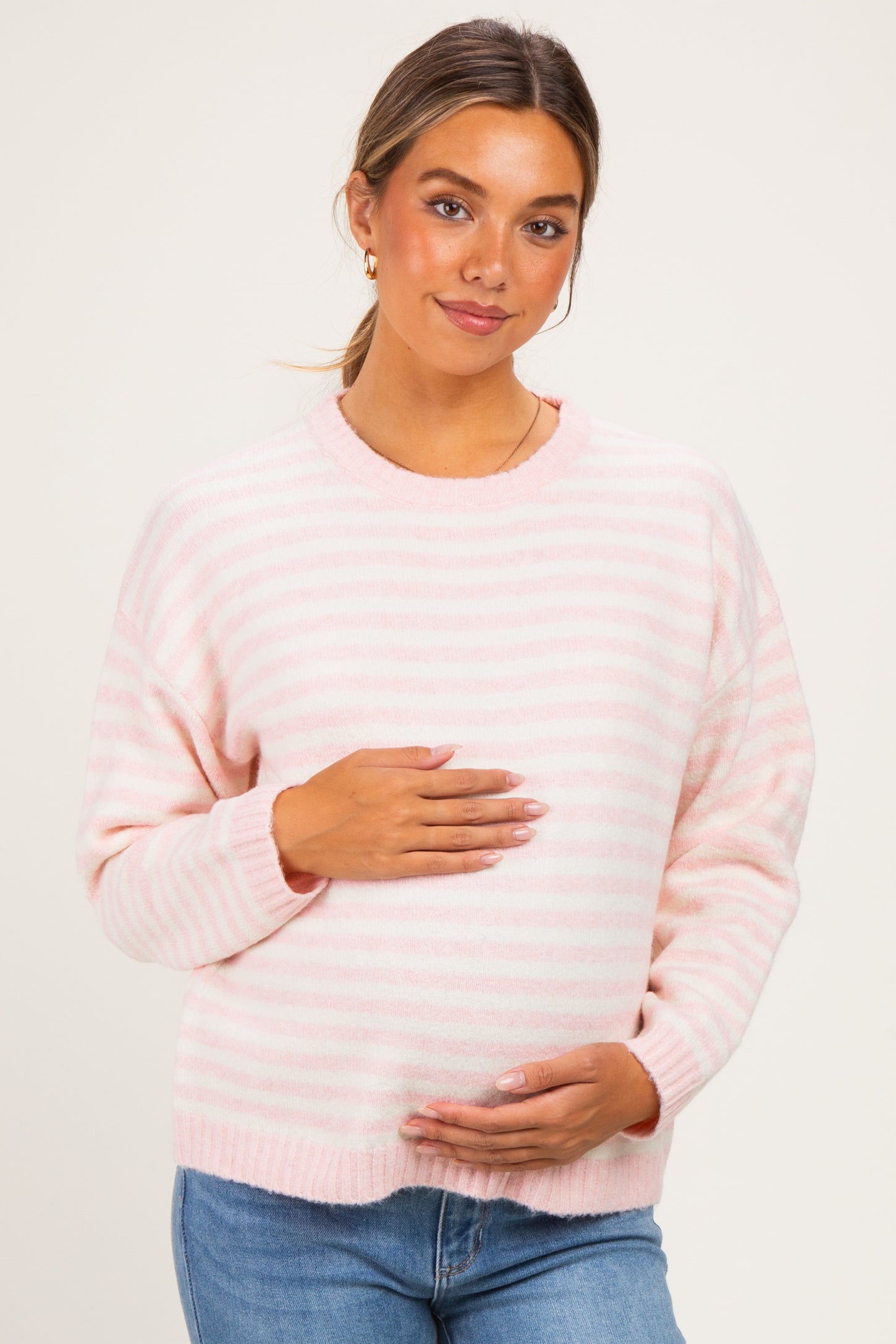 woman wearing a pink and white striped maternity sweater and holding her baby bump