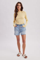 woman wearing a yellow striped long sleeve top and light blue denim shorts with button details