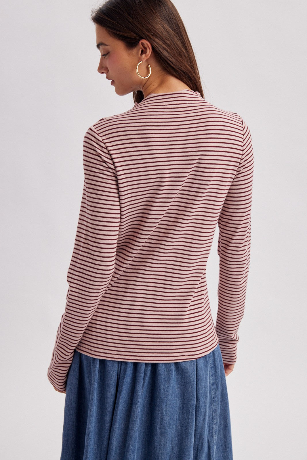 woman wearing a long sleeve striped top in burgundy and pink with a round neckline, styled with a denim skirt