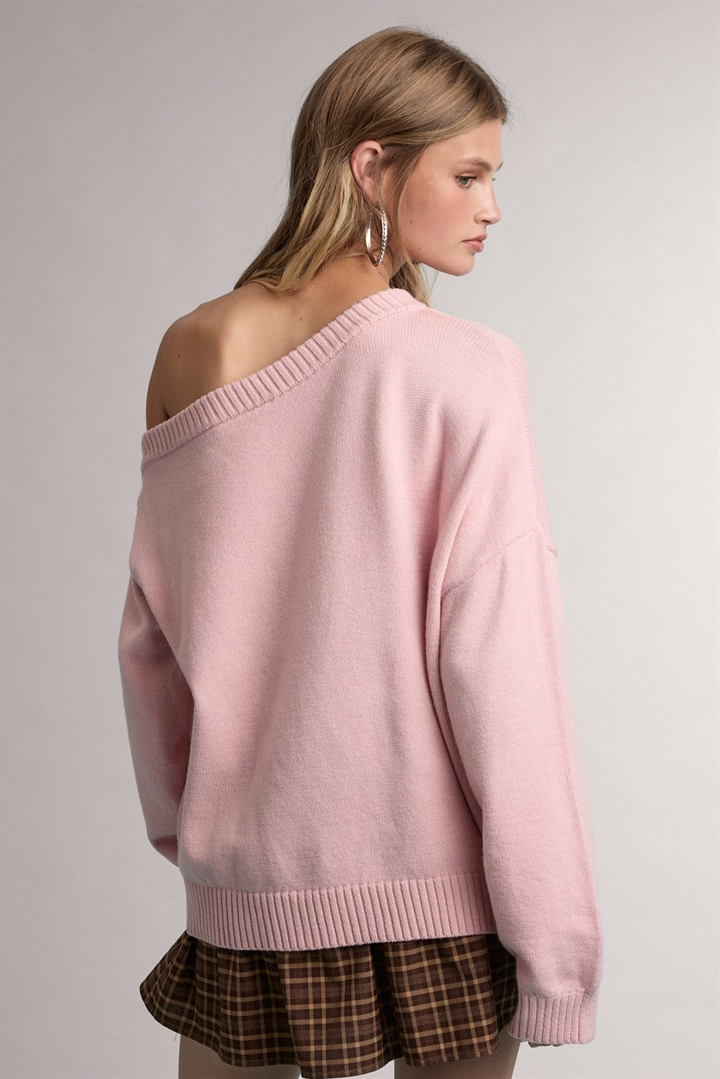 woman wearing a light pink off-shoulder sweater with ribbed hem and back detail, paired with a brown plaid skirt