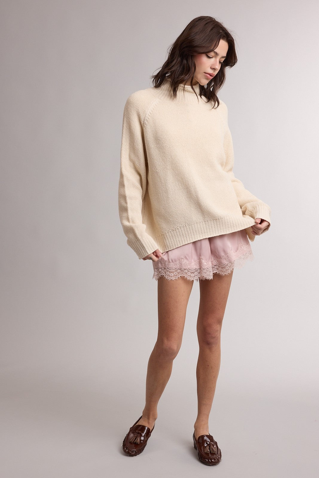 woman wearing a cream-colored oversized sweater with a relaxed fit and matching pink lace trim shorts