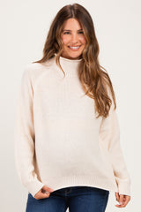woman wearing a light beige maternity sweater with a high neckline and relaxed fit, showing her baby bump