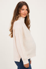 woman wearing a light beige maternity turtleneck sweater and showing her baby bump