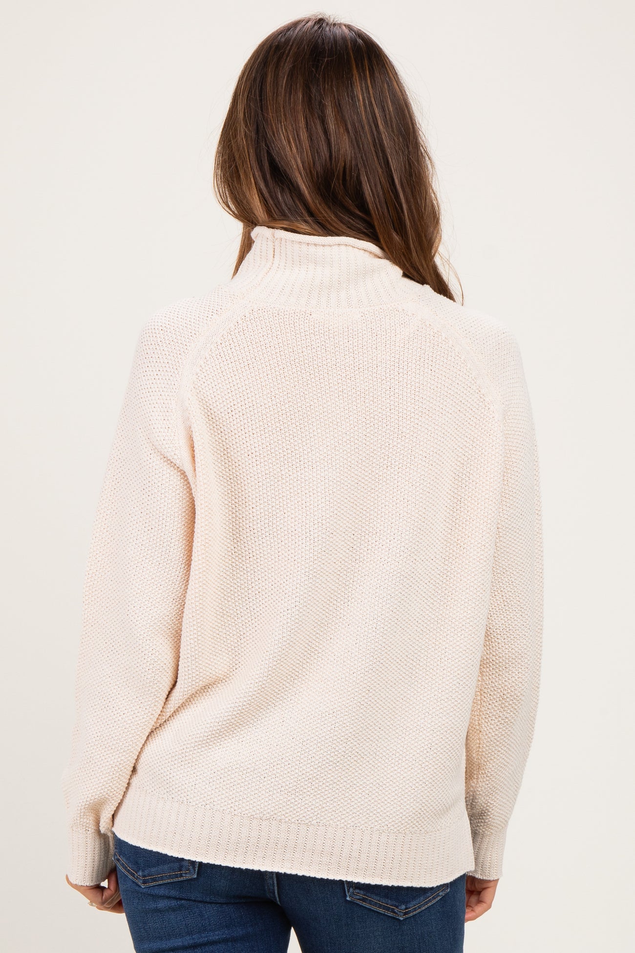 woman wearing a light beige maternity sweater with a high neck and a relaxed fit, shown from the back