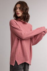 woman wearing a pink oversized sweater with a hood and side slits, styled with casual gray pants