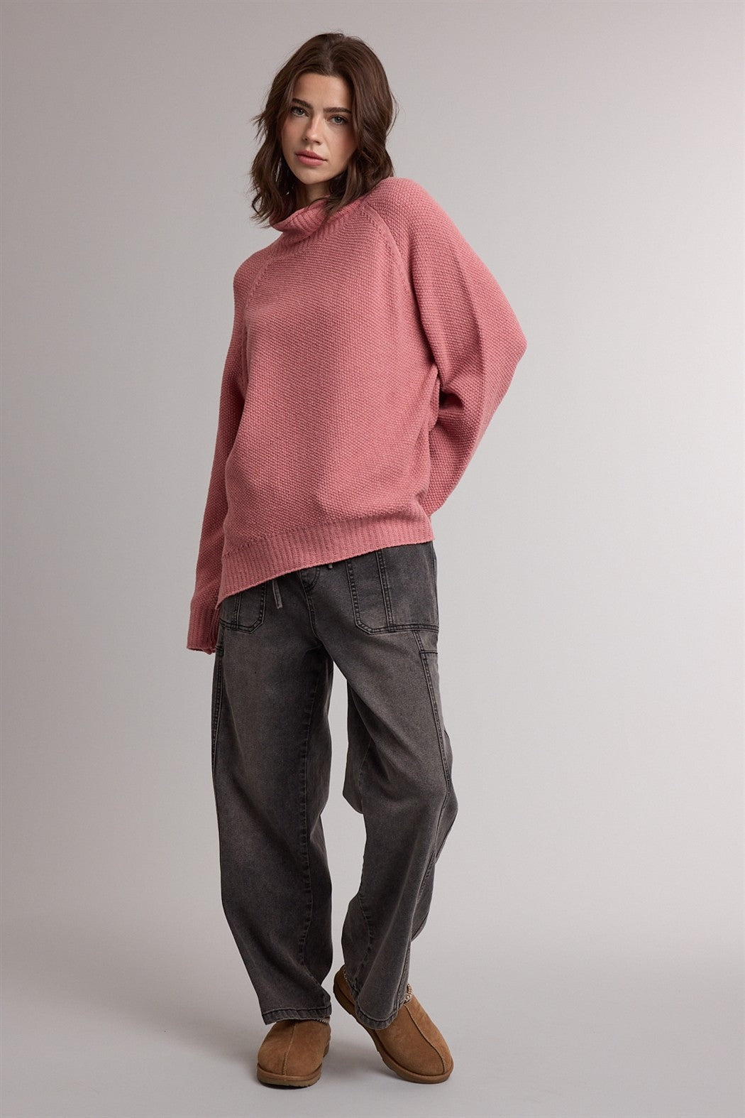 woman wearing a light pink oversized sweater with a crew neck and baggy gray jeans