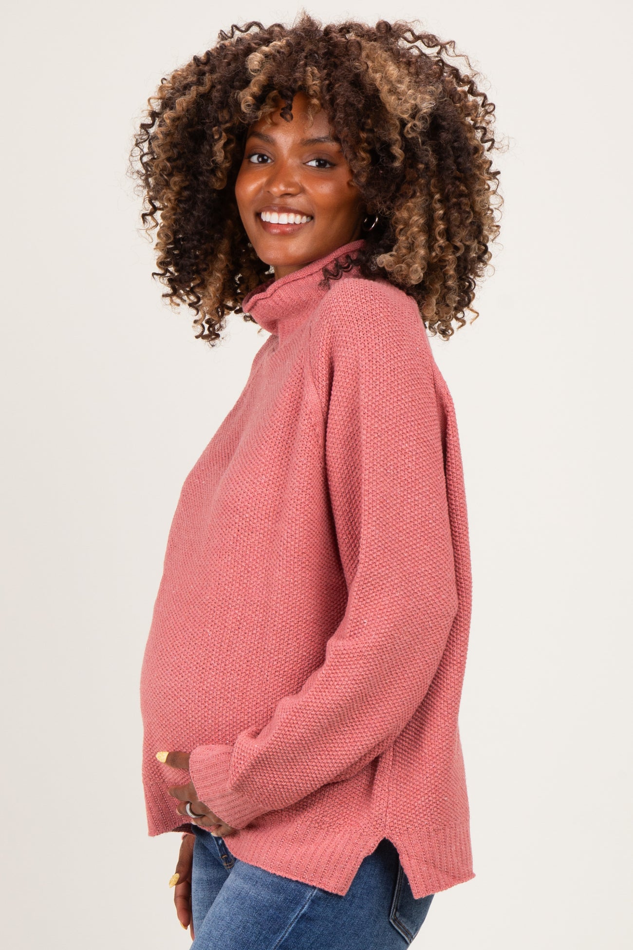 woman wearing a rose pink maternity sweater with a high neck and side slits, highlighting her baby bump