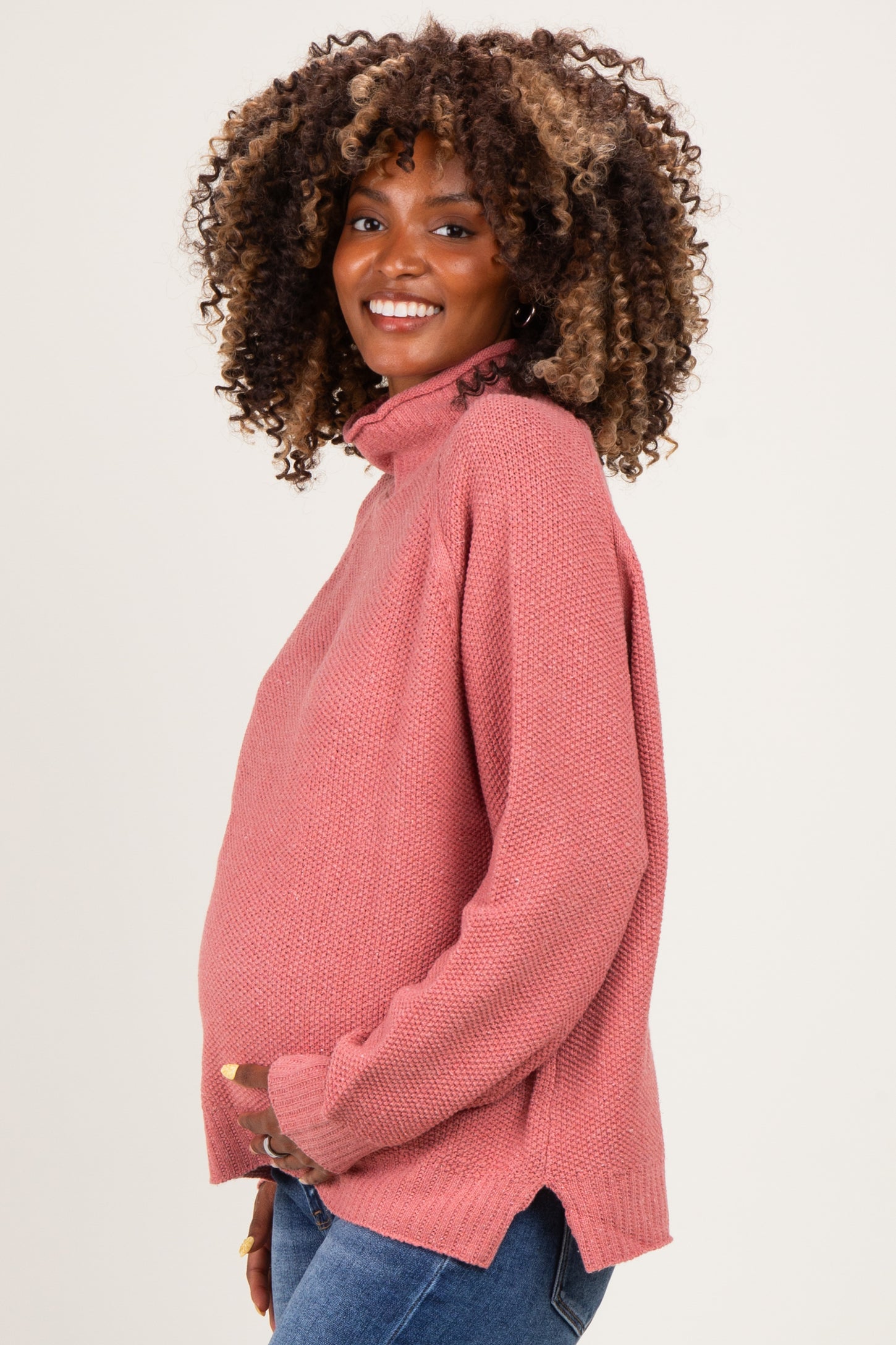 woman wearing a rose pink maternity sweater with a high neck and side slits, highlighting her baby bump