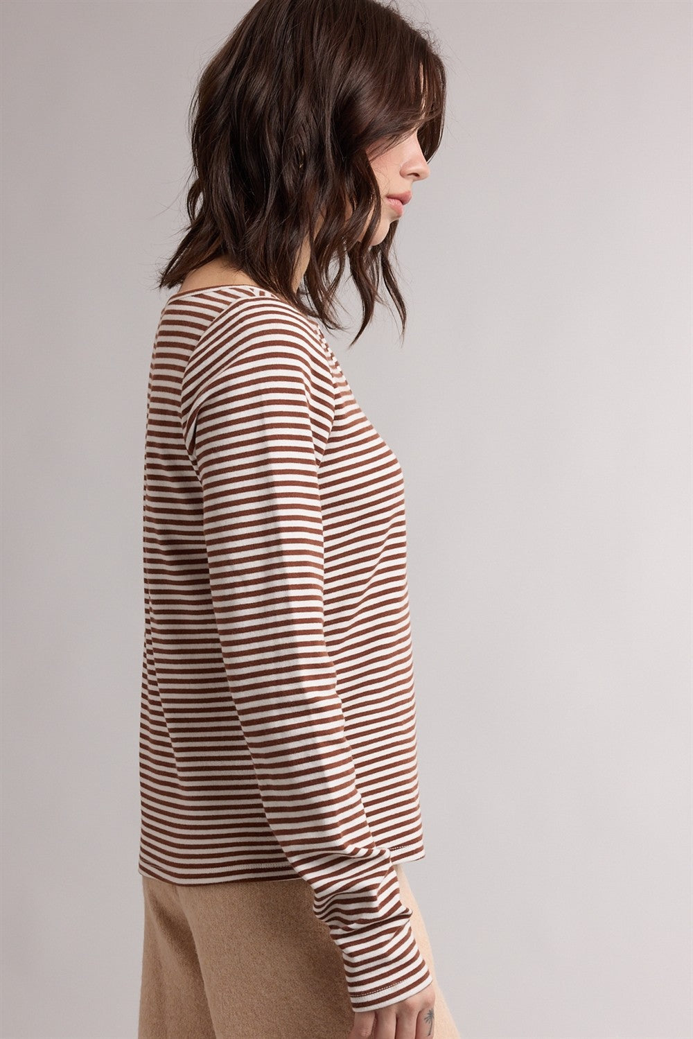 woman wearing a striped long sleeve top in brown and cream, shown from the side