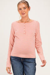 woman wearing a striped maternity top in coral and peach with a henley neckline and long sleeves, showing her baby bump