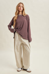 woman wearing a maroon and white striped long sleeve top and cream wide-leg pants, standing on a beige background