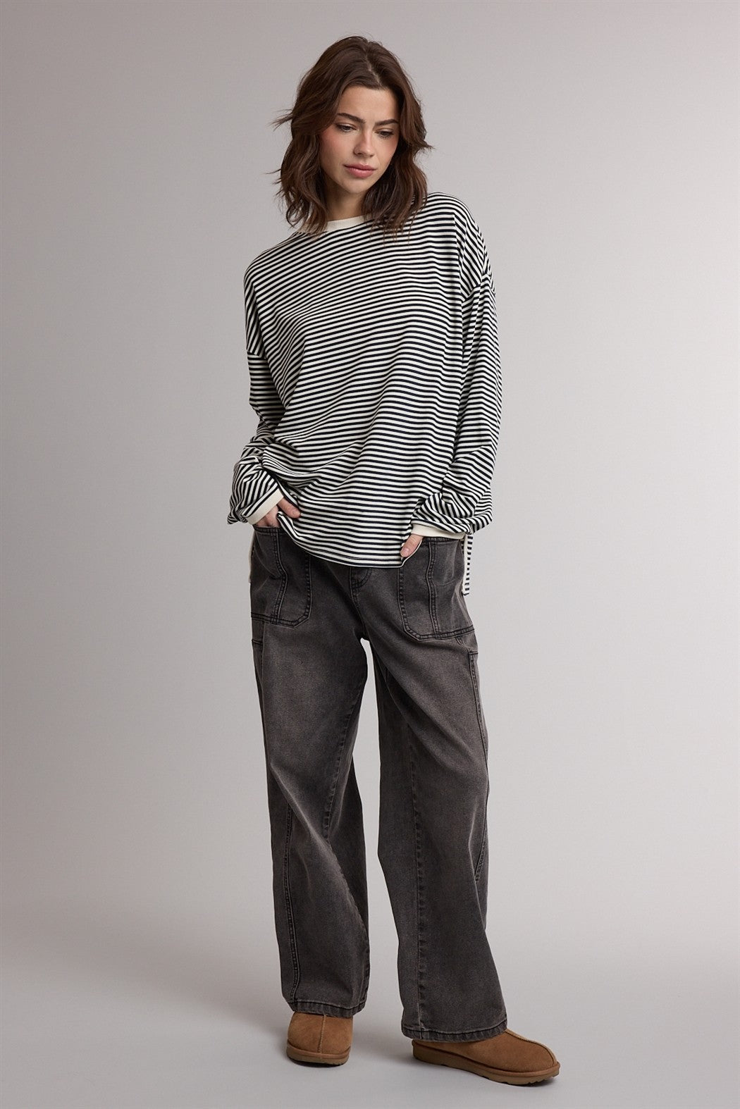 woman wearing a black and white striped oversized long sleeve top with loose gray pants and brown ankle boots