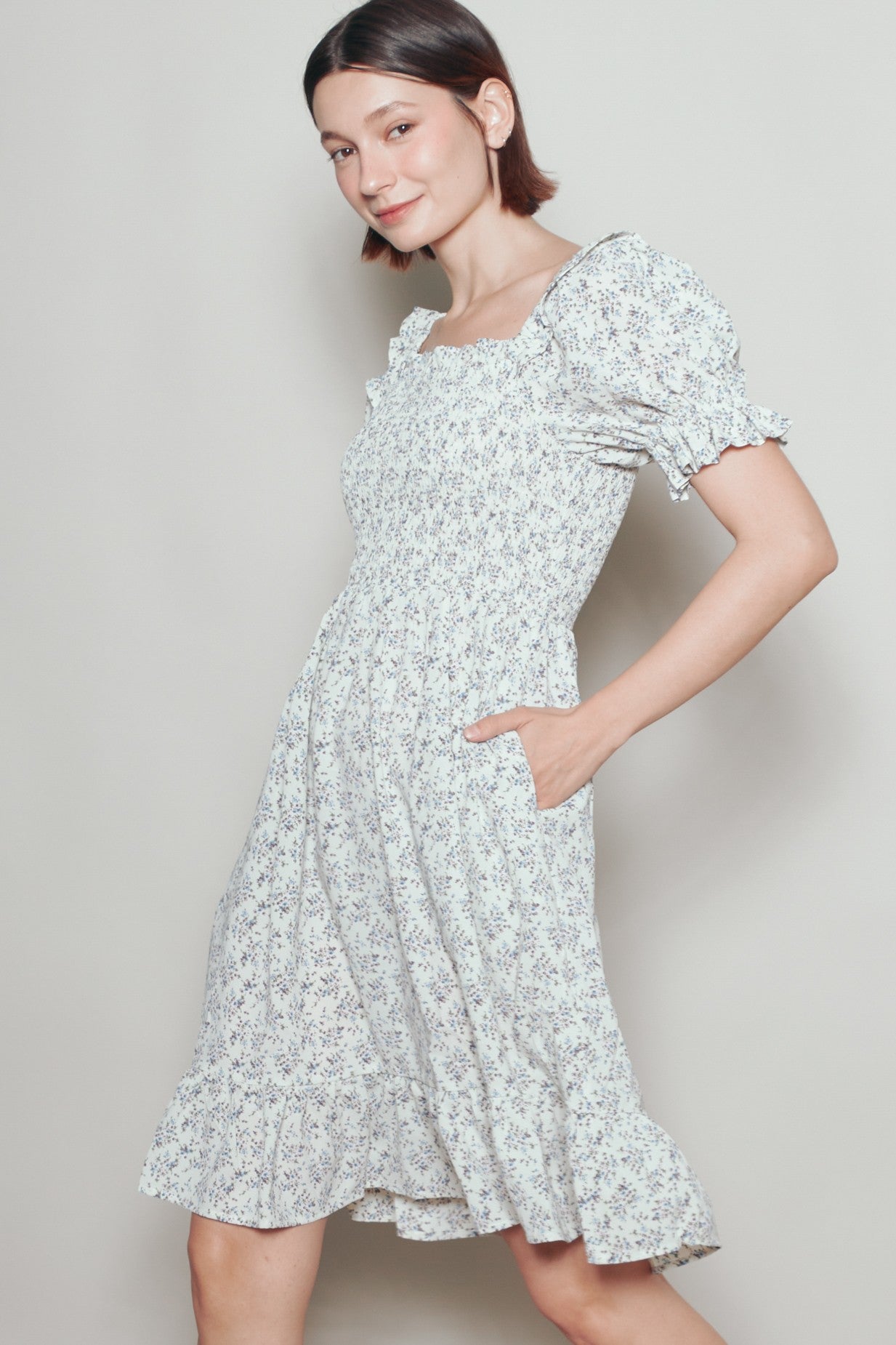woman wearing a white floral midi dress with puff sleeves and pockets, smiling against a light background