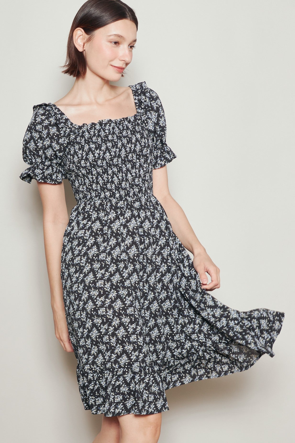 woman wearing a black floral smocked dress with puff sleeves and a square neckline, twirling against a light background