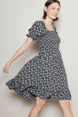 woman wearing a black floral short sleeve dress with a smocked bodice and flared skirt