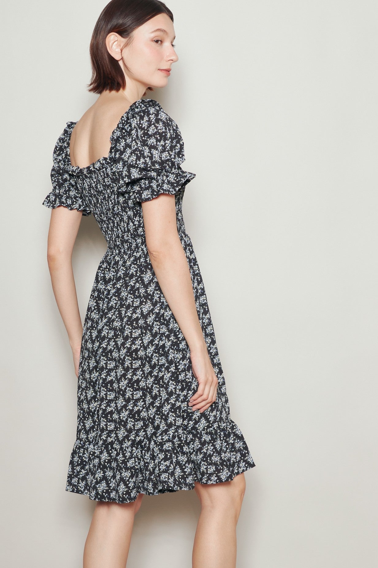 woman wearing a black floral puff sleeve dress with a ruffled hem and a square neckline