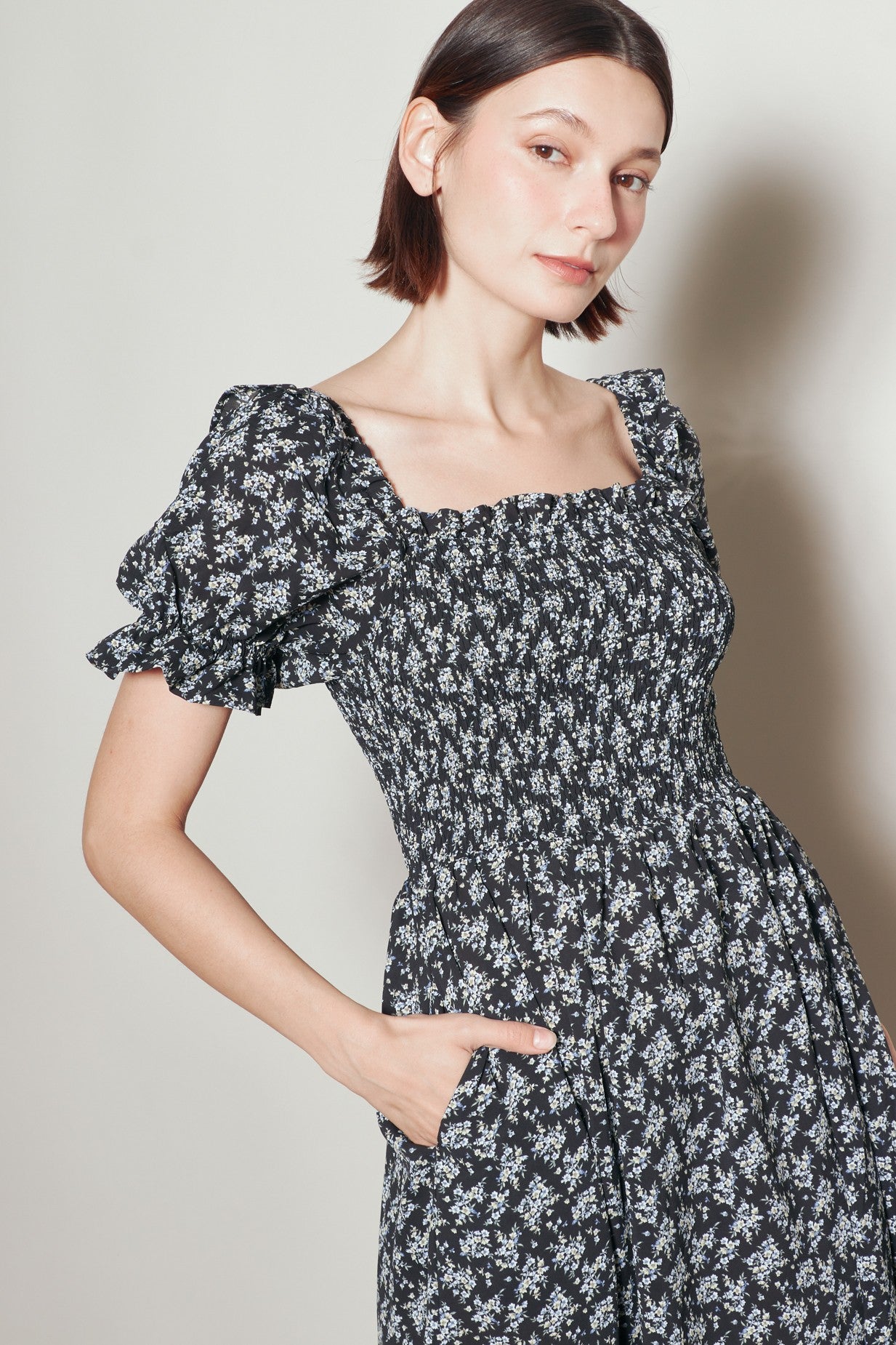 woman wearing a black floral puff sleeve dress with a square neckline and side pockets