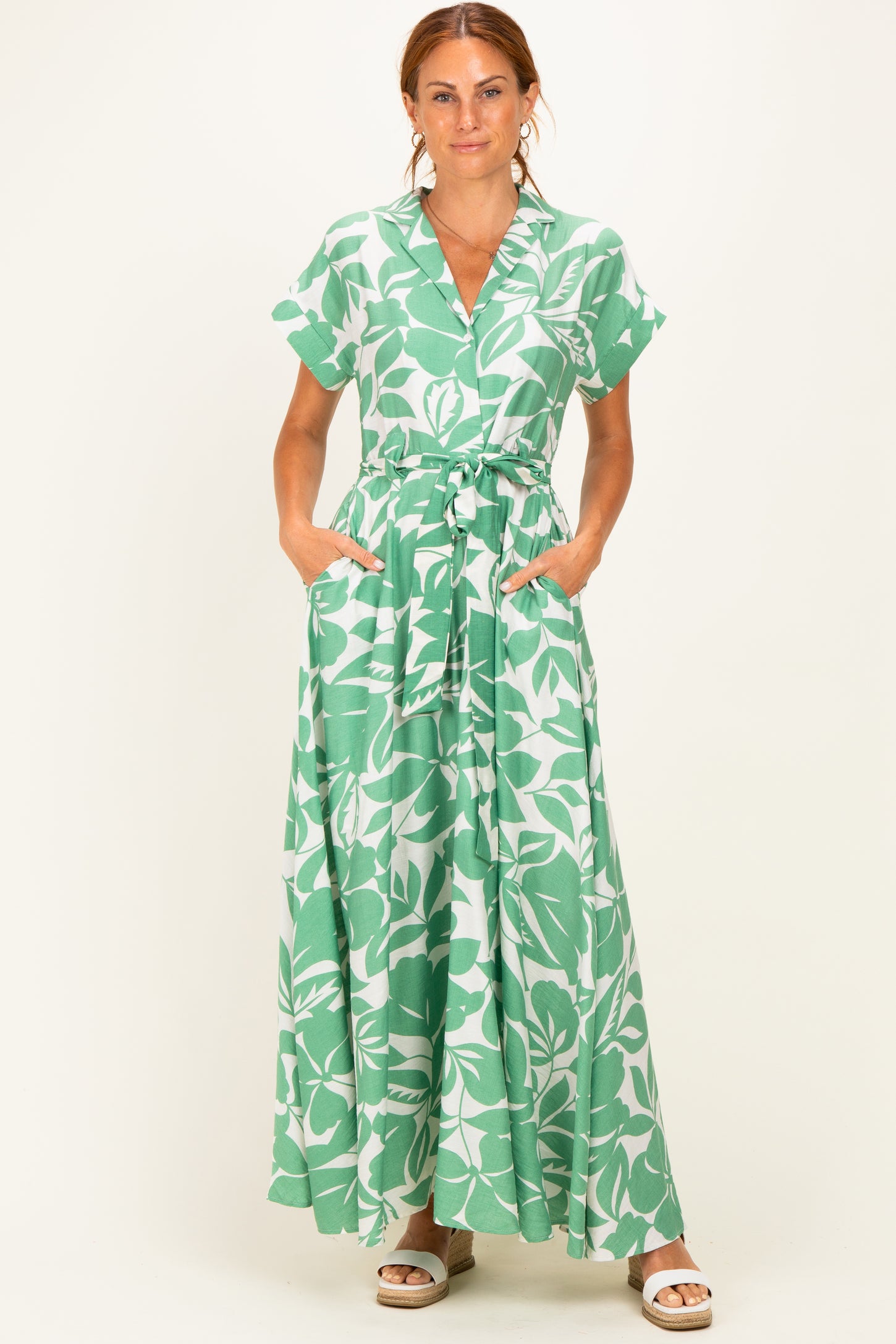 woman wearing a green floral maxi dress with short sleeves and a tied waist, featuring pockets