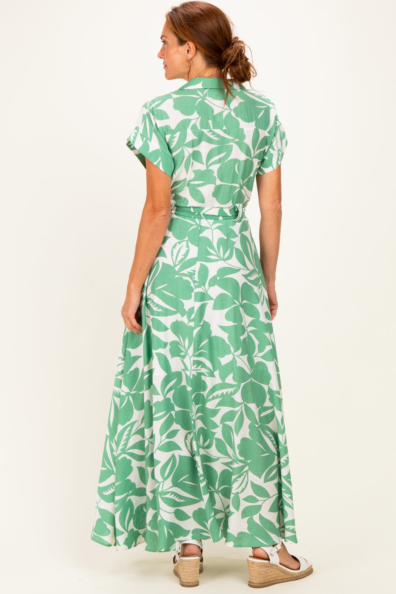 woman wearing a green and white floral maxi dress with short sleeves, showing the back and a flowy hem