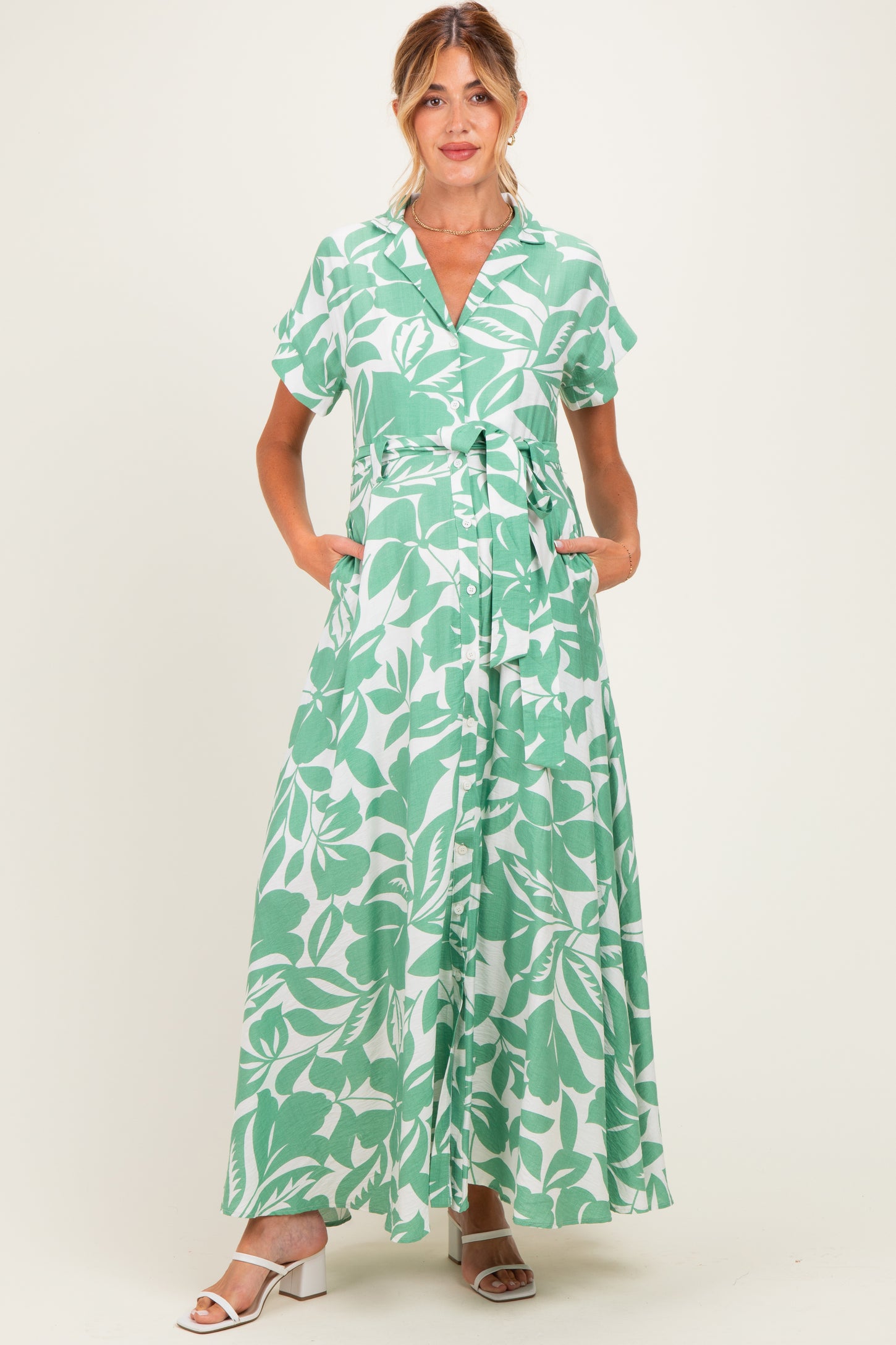 woman wearing a green and white floral maternity maxi dress with short sleeves and a tie waist, pockets visible