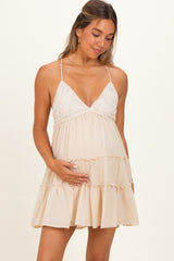 woman wearing a beige maternity dress with lace detail and a tiered skirt, holding her baby bump