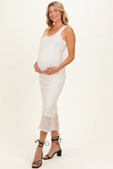 woman wearing a white lace maternity dress and holding her baby bump