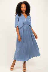 woman wearing a blue pleated maxi dress with a v-neck and short sleeves, standing in heeled sandals