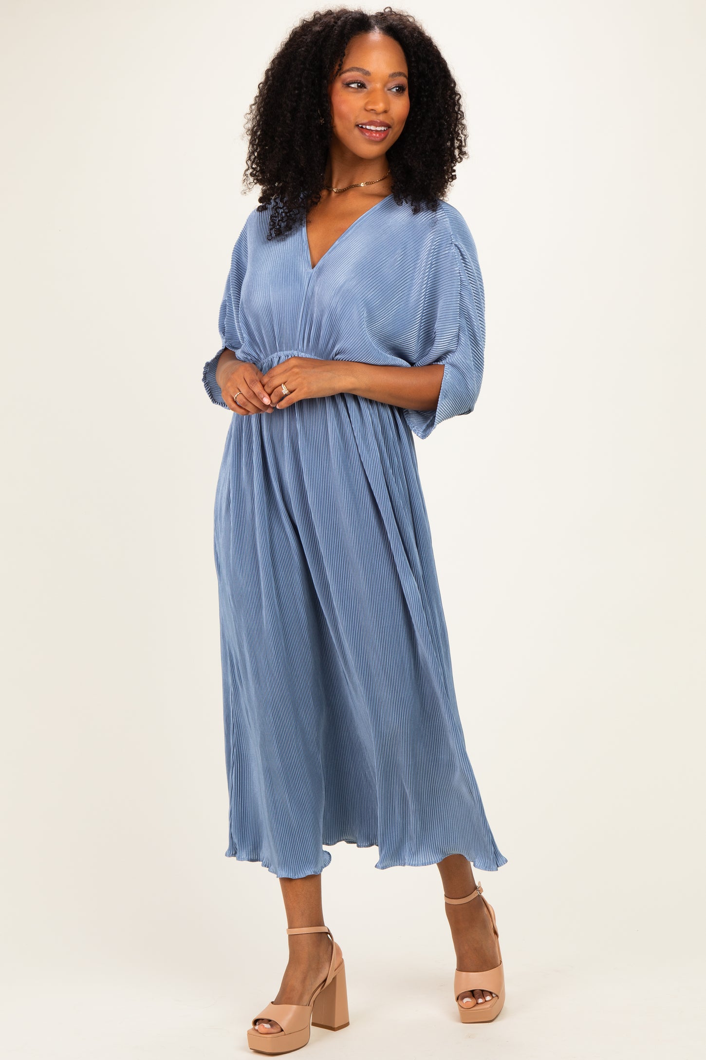 woman wearing a blue v-neck midi dress with pleated fabric and wide sleeves, styled with tan platform heels