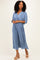 woman wearing a blue v-neck midi dress with pleated fabric and wide sleeves, styled with tan platform heels