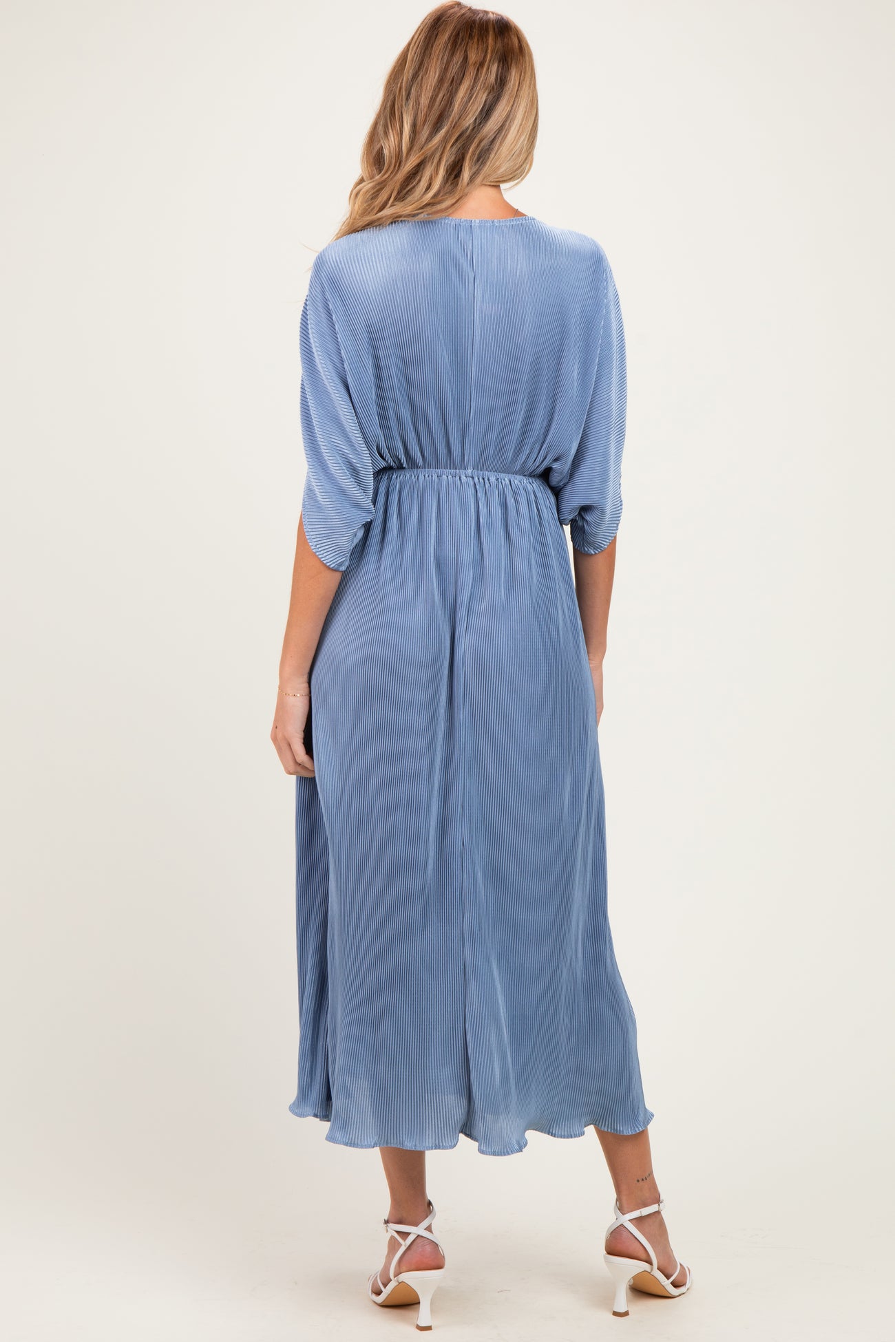 woman wearing a light blue pleated maternity dress with a cinched waist and three-quarter sleeves, showing her baby bump