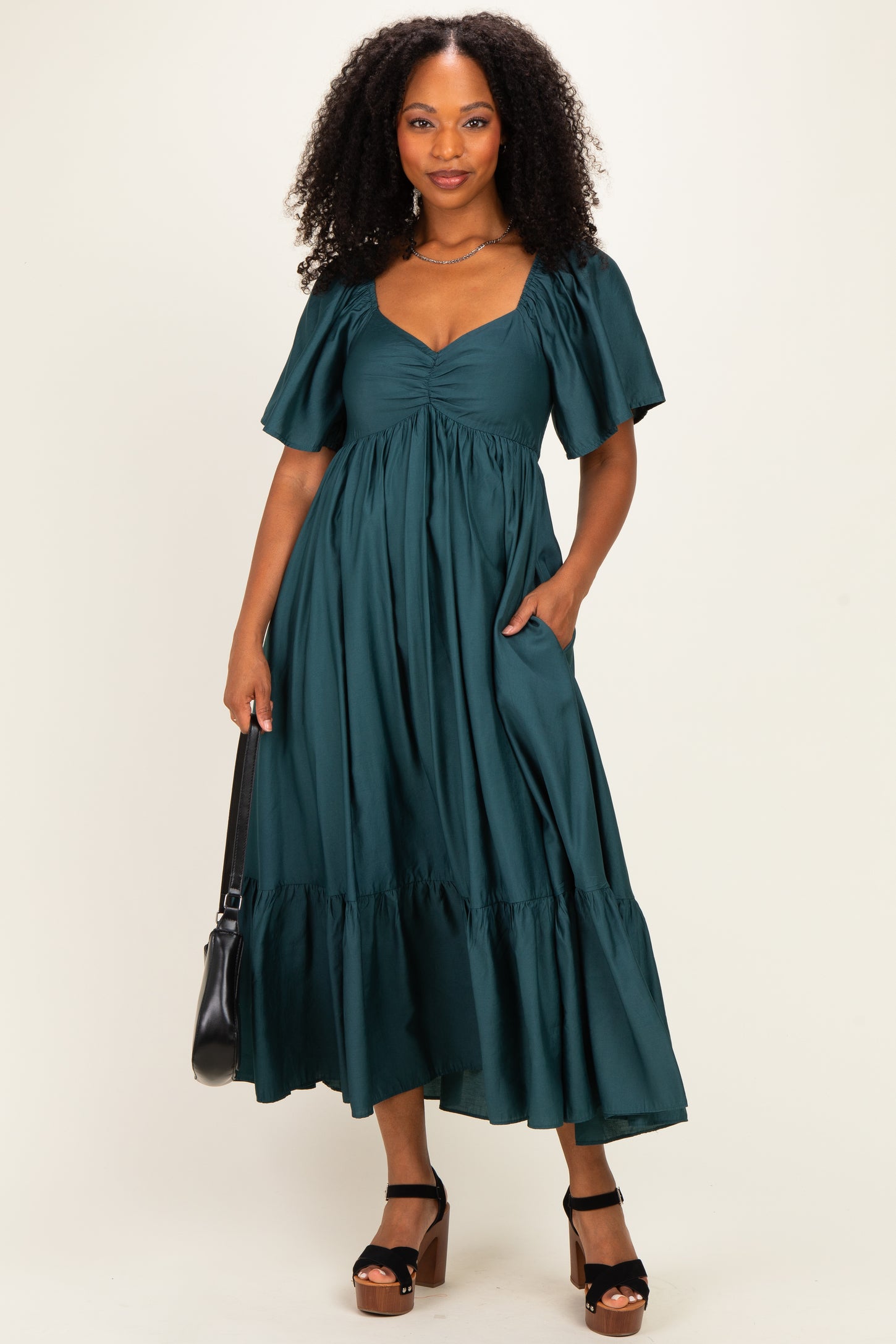 woman wearing a dark green midi dress with puff sleeves and a tiered skirt, holding a black handbag