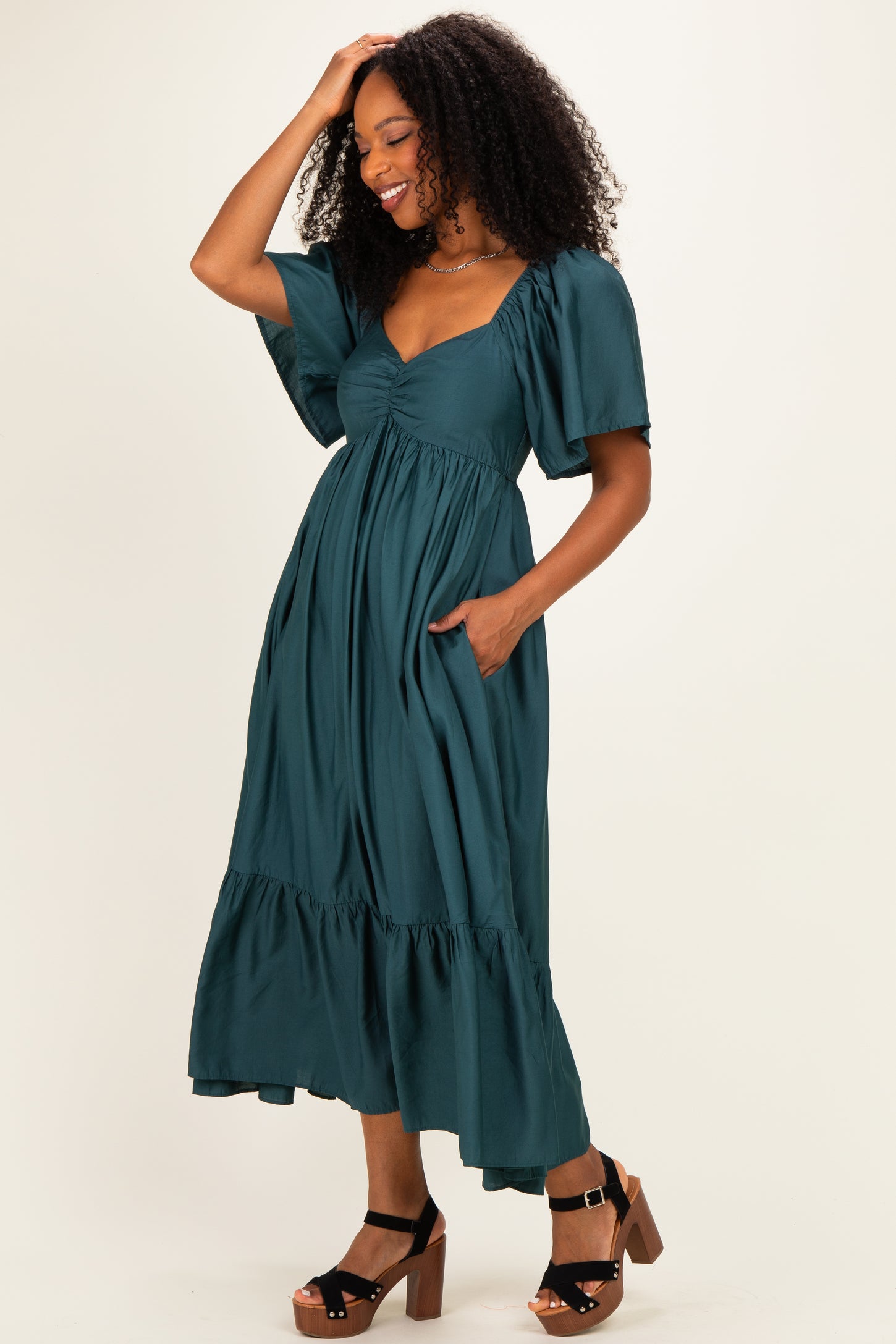 woman wearing a teal maxi dress with puff sleeves, a cinched bodice, and pockets, styled with brown platform sandals
