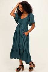 woman wearing a teal maxi dress with puff sleeves, a cinched bodice, and pockets, styled with brown platform sandals