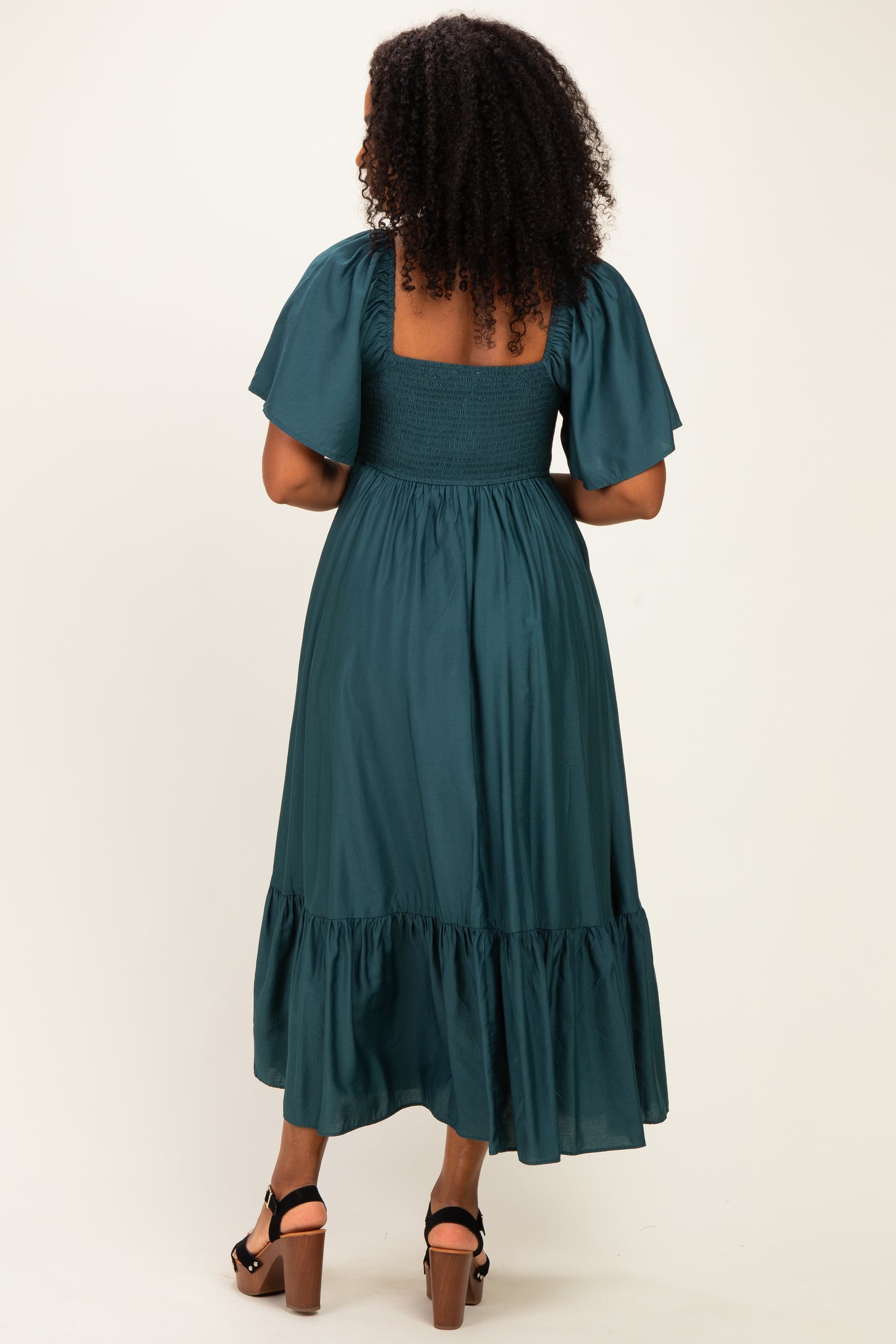 woman wearing a teal midi dress with short puff sleeves and a tiered hem, viewed from the back