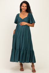 woman wearing a teal maternity dress with short puff sleeves and a tiered skirt, showing her baby bump