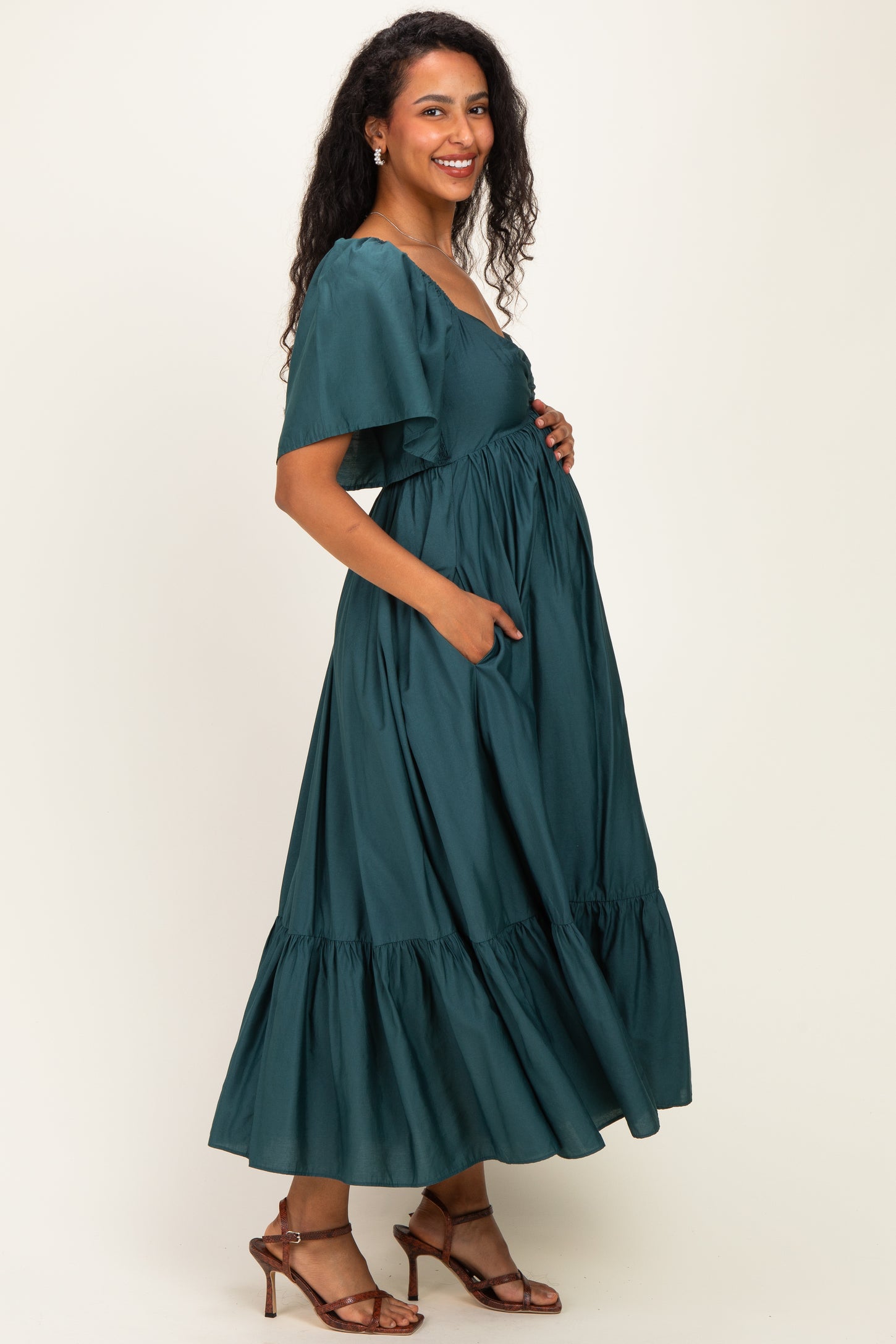 woman wearing a dark green maternity maxi dress with short flutter sleeves and pockets, showing baby bump