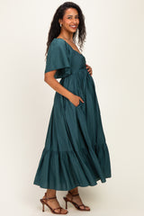 woman wearing a dark green maternity maxi dress with short flutter sleeves and pockets, showing baby bump
