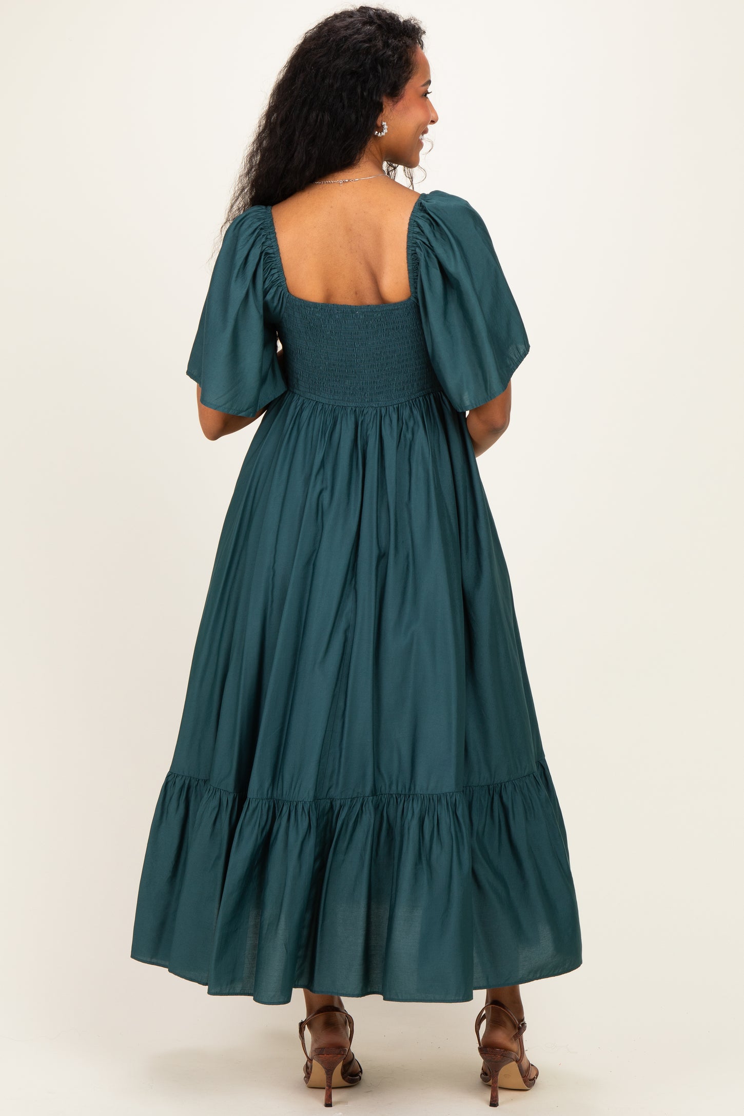 woman wearing a teal maternity dress with puff sleeves and a smocked bodice, featuring a tiered skirt, shown from the back
