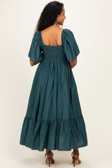 woman wearing a teal maternity dress with puff sleeves and a smocked bodice, featuring a tiered skirt, shown from the back