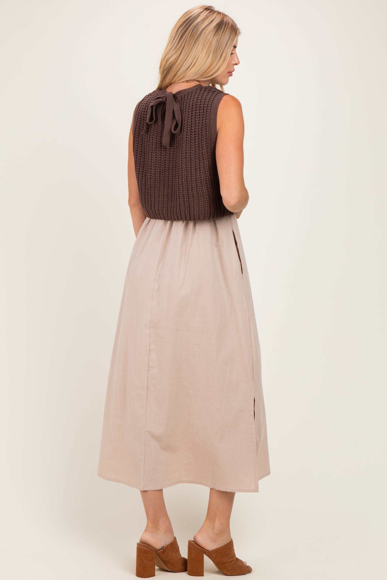 woman wearing a brown knitted top with a back tie and a beige midi skirt, standing with her back facing the camera