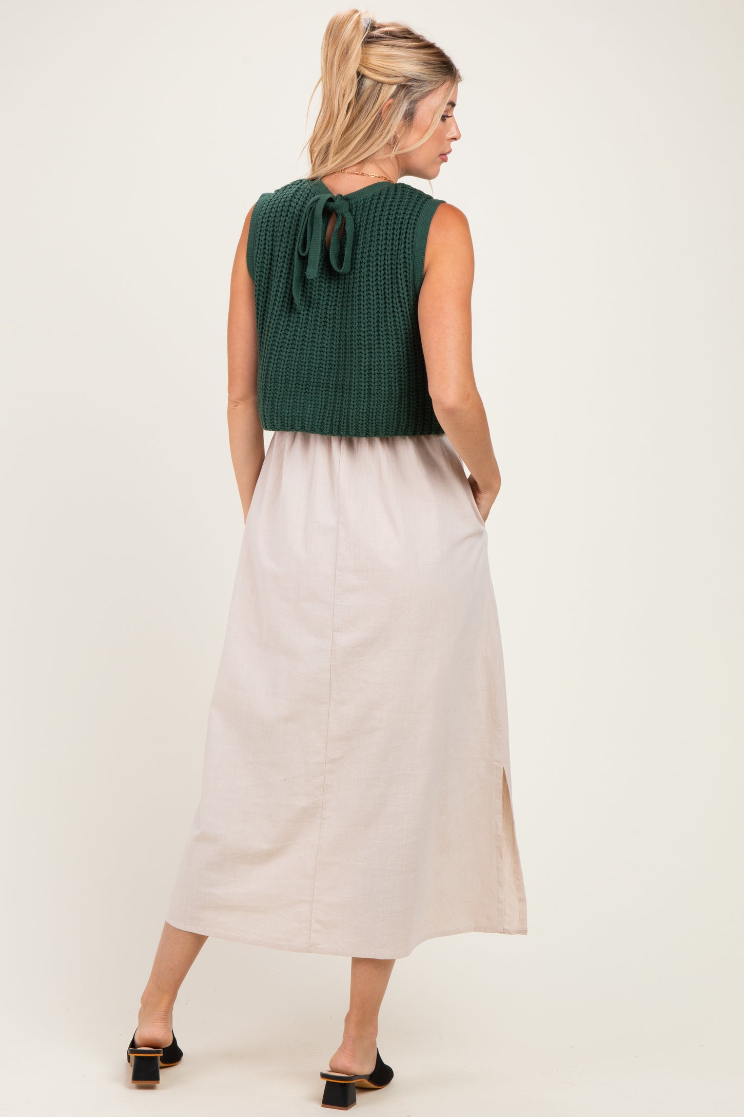 woman wearing a green knitted cropped top over a beige maxi dress with side pockets and a slit detail