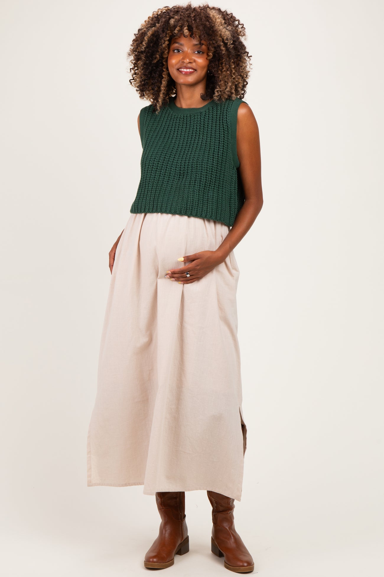 woman wearing a dark green knitted crop top and a light beige maxi skirt, showcasing her baby bump in maternity wear
