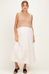 woman wearing a beige knitted crop top over a white maxi maternity dress, featuring a baby bump