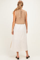 woman wearing a beige knitted maternity vest over a long white linen dress, showing a relaxed style with a back tie detail