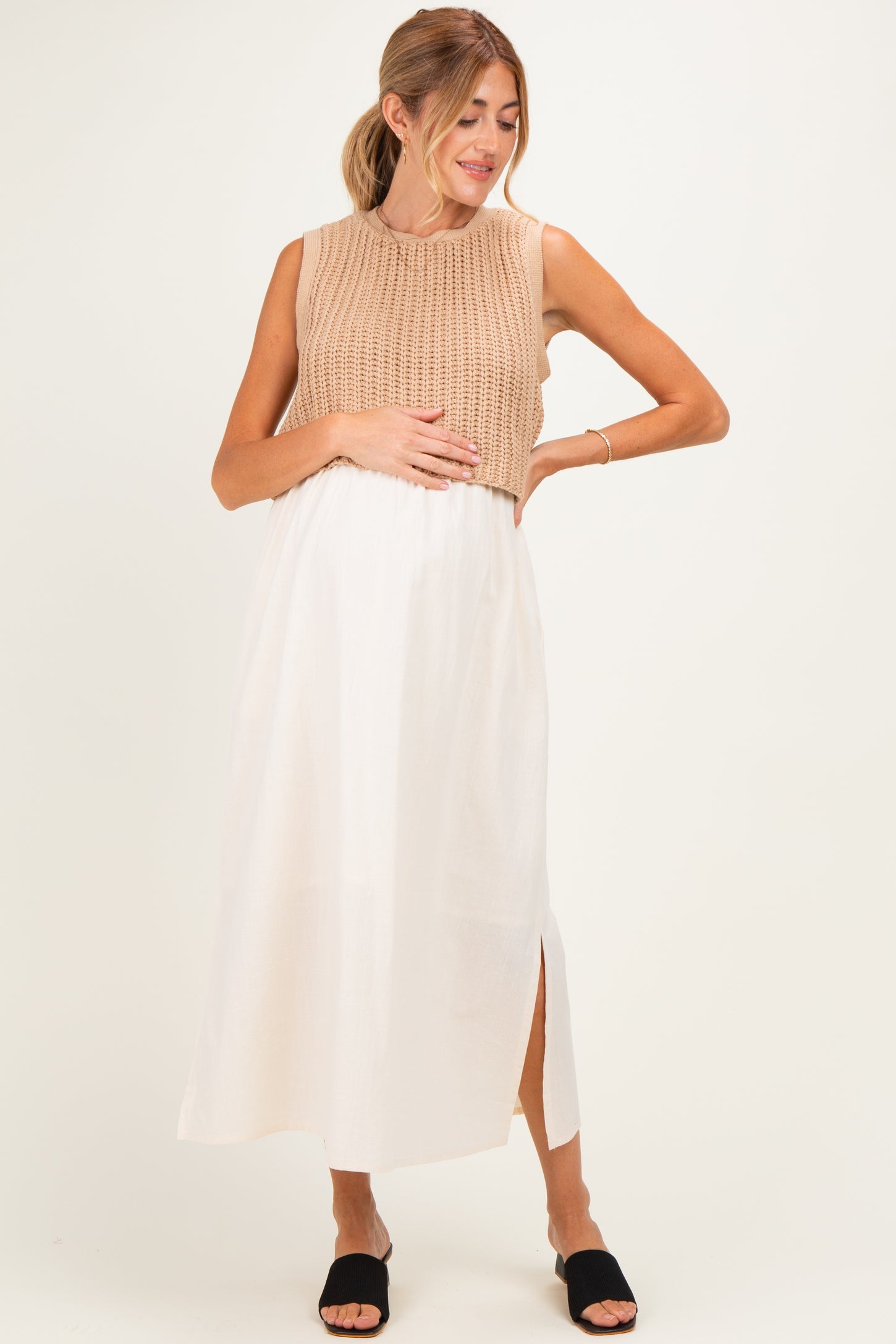 woman wearing a beige sleeveless sweater and a white maxi skirt, showing her baby bump as maternity wear