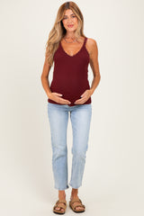 woman wearing a burgundy maternity tank top with lace trim and holding her baby bump, paired with light wash jeans