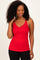woman wearing a red scalloped edge tank top and black leggings, smiling and touching her hair