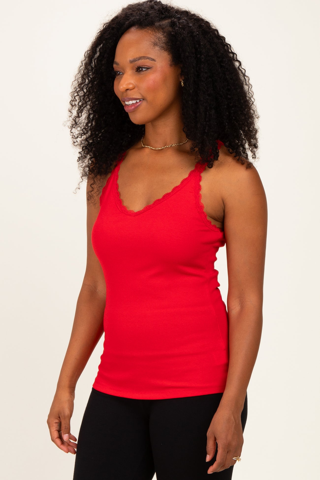 woman wearing a red lacy edge tank top paired with black leggings and smiling at the side