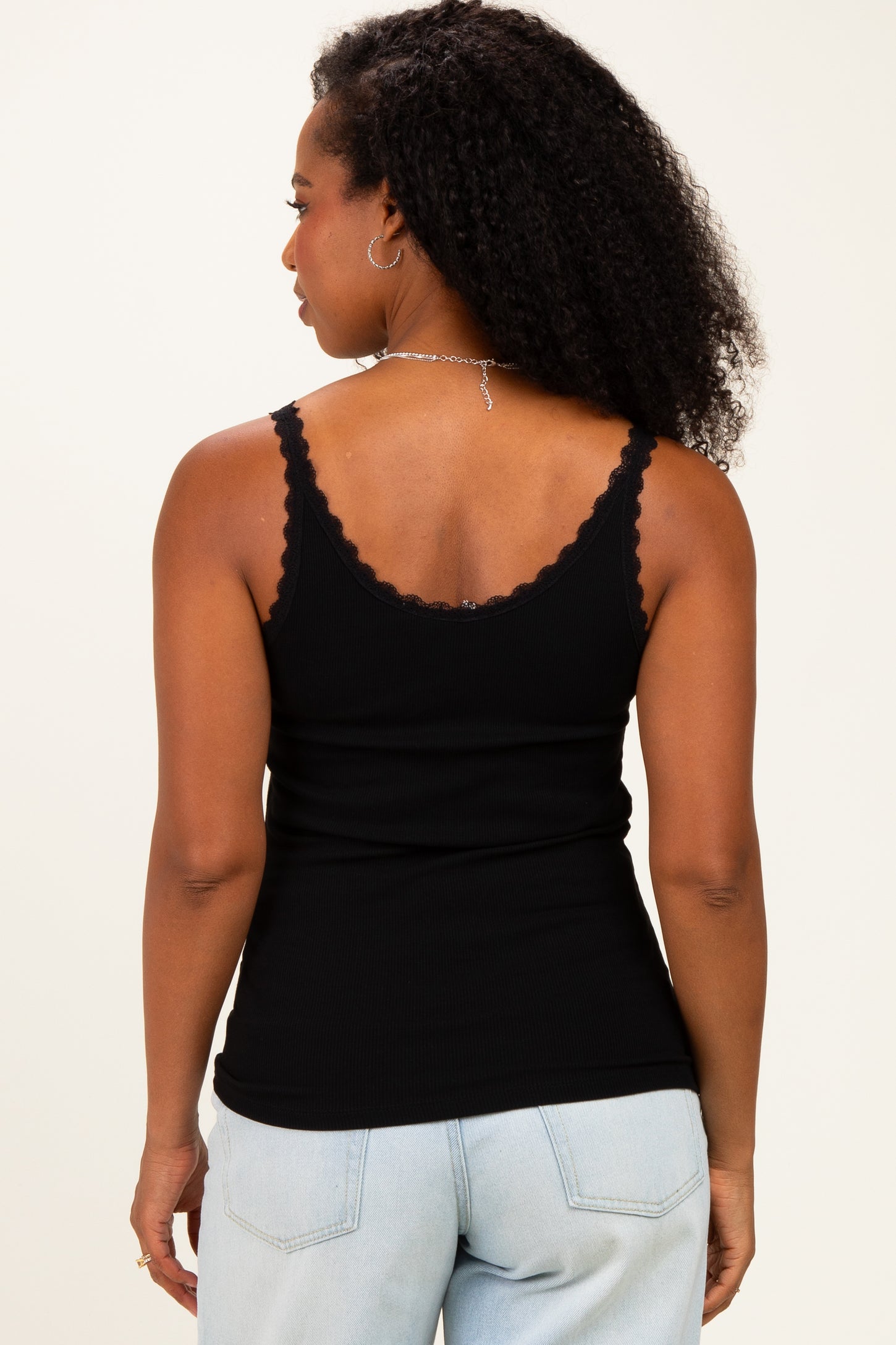 woman wearing a black scoop neck tank top with scalloped edges and spaghetti straps, viewed from the back