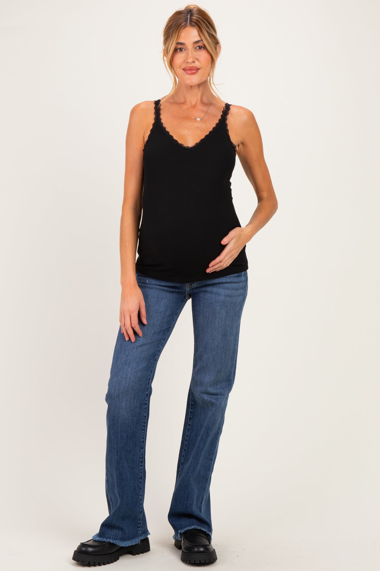 woman wearing a black maternity tank top and blue jeans, gently cradling her baby bump